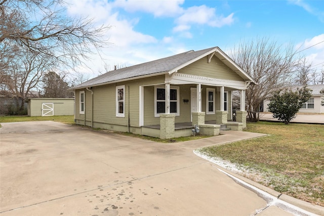 bungalow-style home featuring an outbuilding, covered porch, a front lawn, a storage unit, and driveway