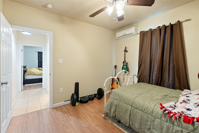 bedroom featuring ceiling fan, an AC wall unit, a textured ceiling, and light wood-type flooring