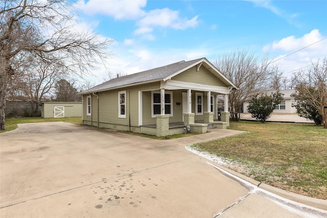 bungalow-style home featuring an outbuilding, a porch, a front lawn, driveway, and a storage unit