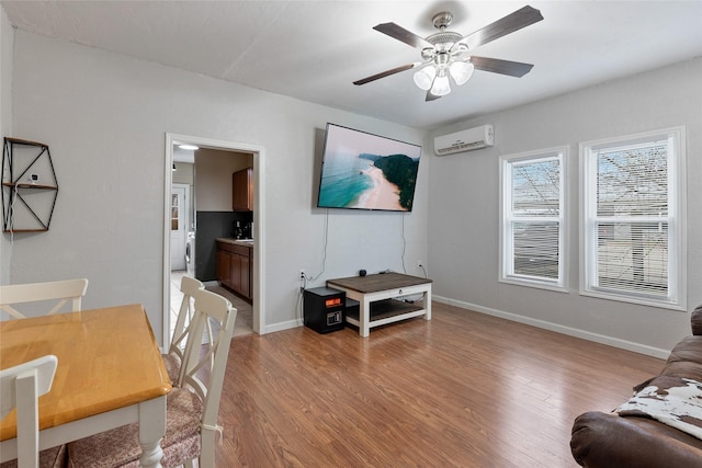 living area with a wall mounted AC, a ceiling fan, baseboards, and light wood-style floors