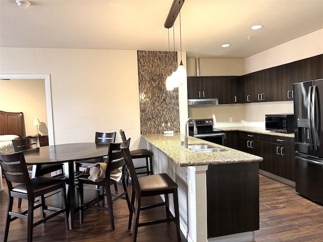 kitchen with dark brown cabinetry, dark wood-style floors, a peninsula, black appliances, and a sink