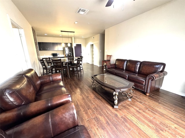 living room with dark wood-type flooring, visible vents, and ceiling fan