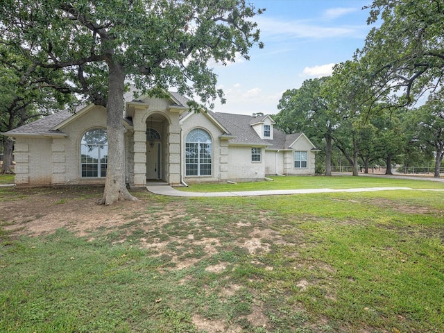 view of front of property featuring a shingled roof, brick siding, and a front lawn