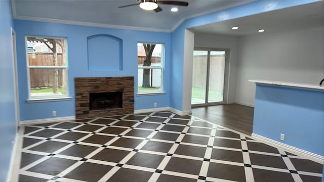 unfurnished living room with ceiling fan, ornamental molding, a stone fireplace, and dark wood-type flooring