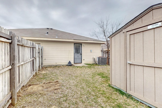 rear view of property with roof with shingles, a lawn, a fenced backyard, and central air condition unit