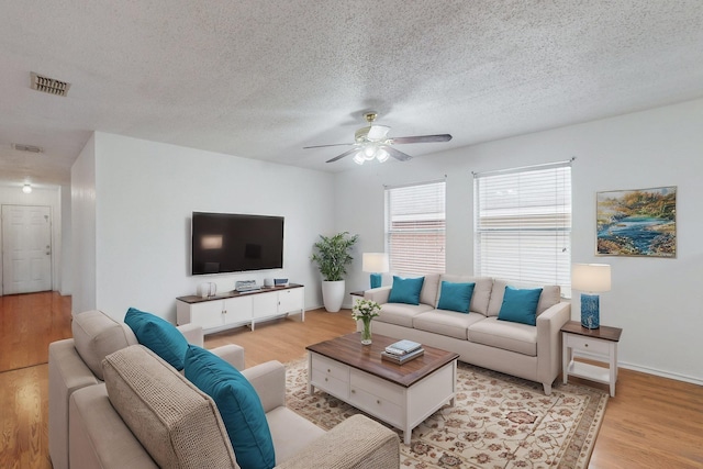 living room with ceiling fan, a textured ceiling, light wood-style flooring, visible vents, and baseboards