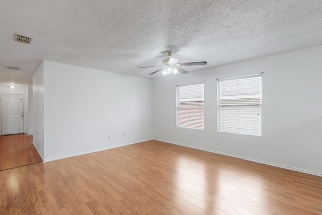 spare room with baseboards, visible vents, light wood-style flooring, ceiling fan, and a textured ceiling