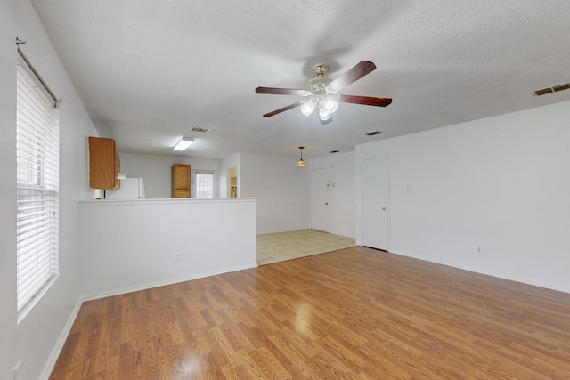 unfurnished living room with a textured ceiling, ceiling fan, light wood finished floors, and visible vents