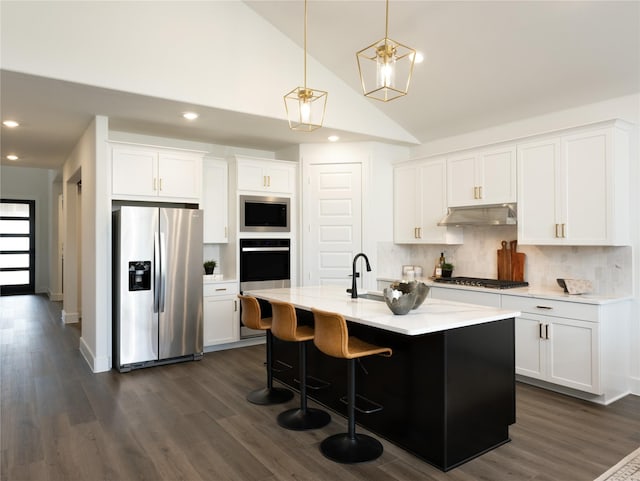 kitchen featuring appliances with stainless steel finishes, decorative light fixtures, an island with sink, and white cabinets