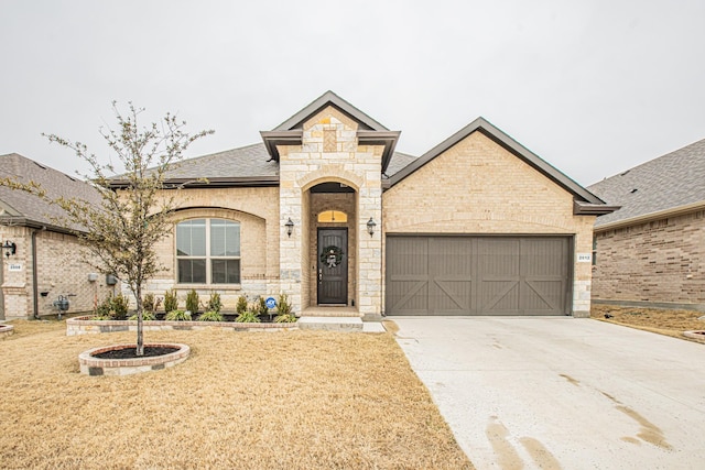 french country home featuring brick siding, concrete driveway, roof with shingles, a garage, and stone siding