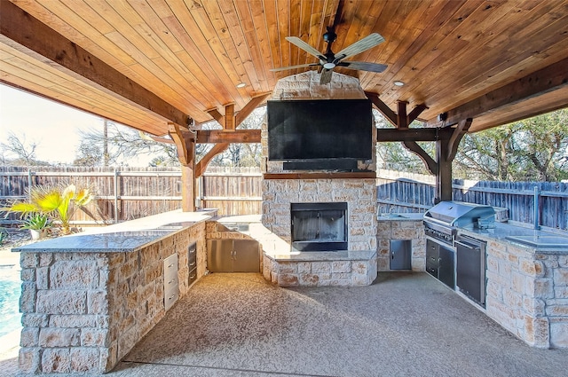 view of patio with ceiling fan, an outdoor stone fireplace, area for grilling, and exterior kitchen