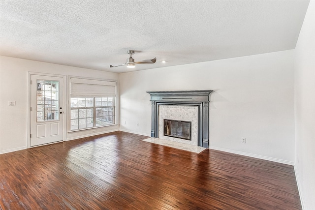 unfurnished living room with ceiling fan, a premium fireplace, dark wood-type flooring, and a textured ceiling