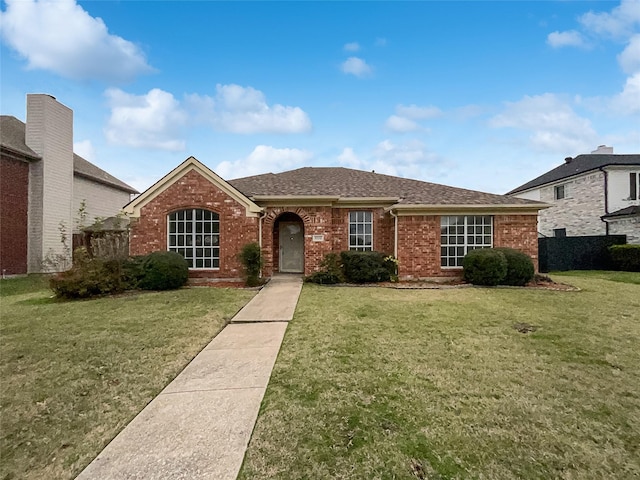 single story home featuring roof with shingles, a front yard, and brick siding