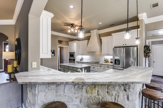 kitchen featuring appliances with stainless steel finishes, custom range hood, decorative light fixtures, white cabinetry, and kitchen peninsula