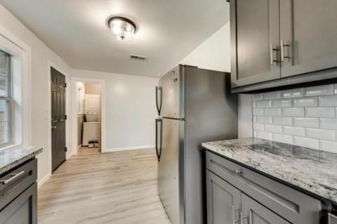 kitchen with stainless steel refrigerator, light stone countertops, backsplash, and gray cabinetry