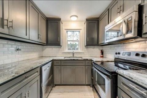 kitchen featuring gray cabinetry, sink, light stone counters, appliances with stainless steel finishes, and decorative backsplash