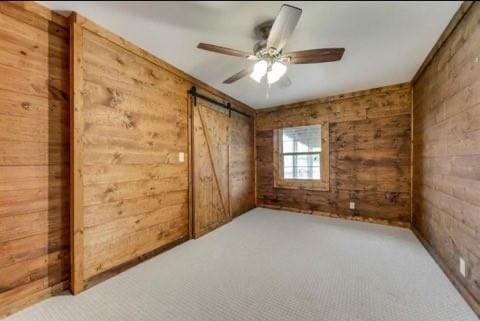 spare room with ceiling fan, wooden walls, a barn door, and carpet floors