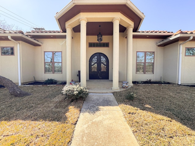 property entrance featuring stucco siding, a tile roof, a lawn, and french doors