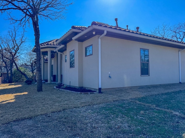 view of property exterior with a lawn, a tile roof, and stucco siding