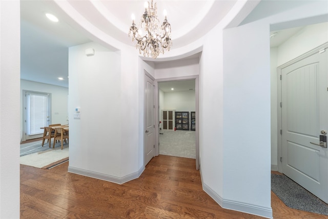 hall with a notable chandelier, a raised ceiling, and hardwood / wood-style floors