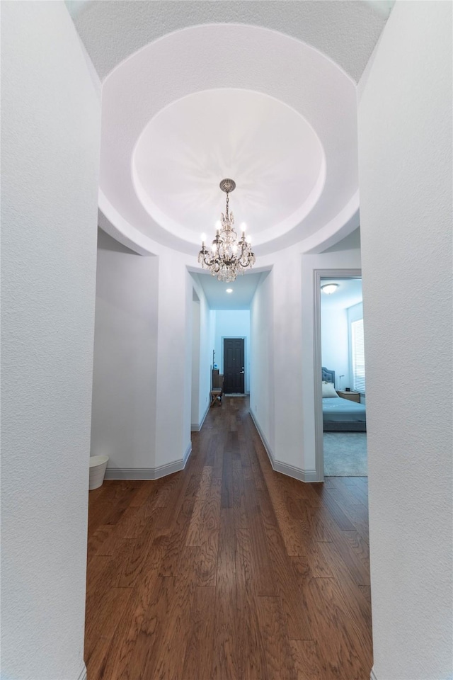 hallway with a notable chandelier, a raised ceiling, and dark hardwood / wood-style floors