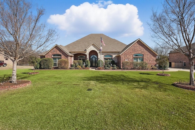 view of front of property with a shingled roof, a front yard, and brick siding