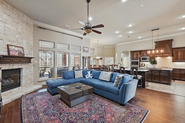 living room featuring crown molding, ceiling fan with notable chandelier, a fireplace, and arched walkways