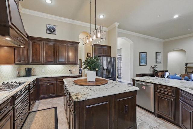 kitchen featuring arched walkways, ornamental molding, a kitchen island, appliances with stainless steel finishes, and backsplash