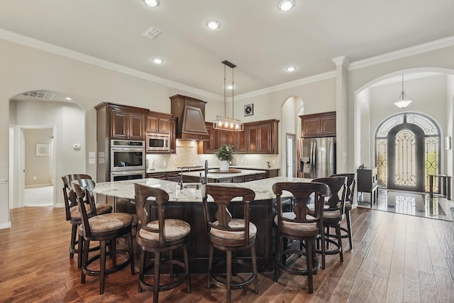 kitchen with arched walkways, visible vents, a large island, stainless steel appliances, and premium range hood