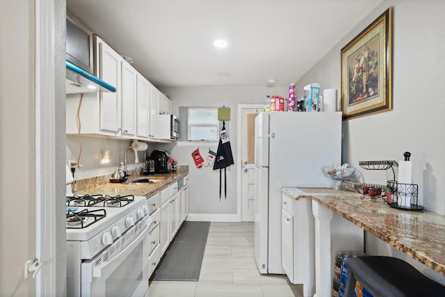 kitchen with white appliances, light stone countertops, white cabinets, range hood, and sink