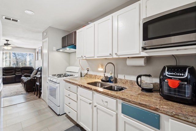 kitchen with light stone counters, ceiling fan, sink, white cabinetry, and white gas range oven