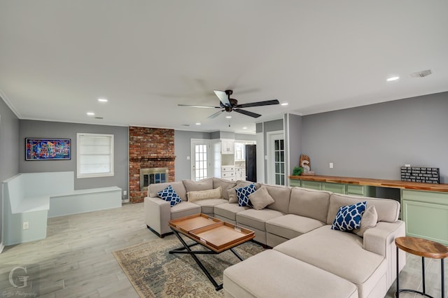 living room with light wood-type flooring, ceiling fan, crown molding, and a fireplace