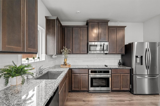 kitchen with appliances with stainless steel finishes, light hardwood / wood-style flooring, light stone counters, decorative backsplash, and sink