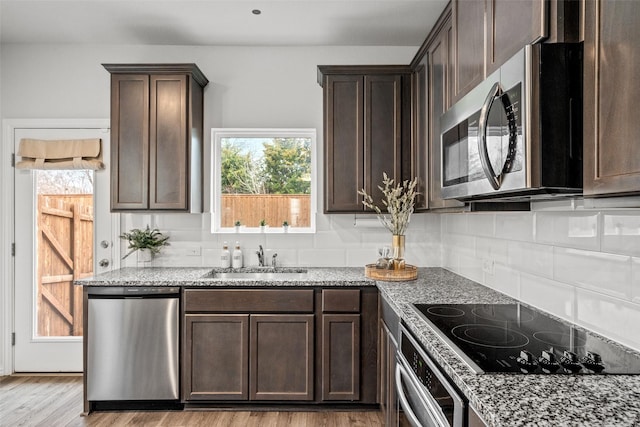 kitchen featuring light wood-type flooring, light stone countertops, sink, dark brown cabinets, and appliances with stainless steel finishes