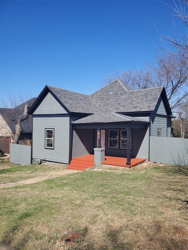 view of front of home featuring covered porch, roof with shingles, fence, and a front yard