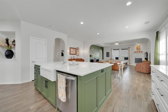 kitchen with arched walkways, dishwasher, a fireplace, green cabinets, and a sink