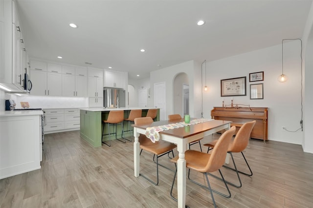 dining area with arched walkways, light wood-style floors, and recessed lighting