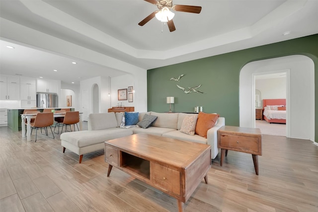 living room featuring arched walkways, light wood finished floors, recessed lighting, a raised ceiling, and a ceiling fan