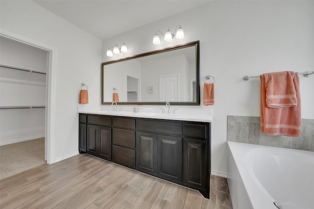 full bath with double vanity, a garden tub, a spacious closet, and a sink