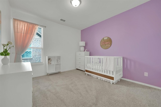 unfurnished bedroom featuring a nursery area, carpet flooring, visible vents, and baseboards