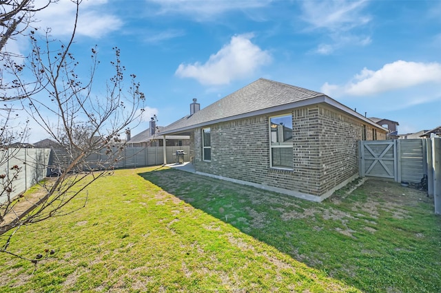 rear view of property with a yard, brick siding, a fenced backyard, and a gate