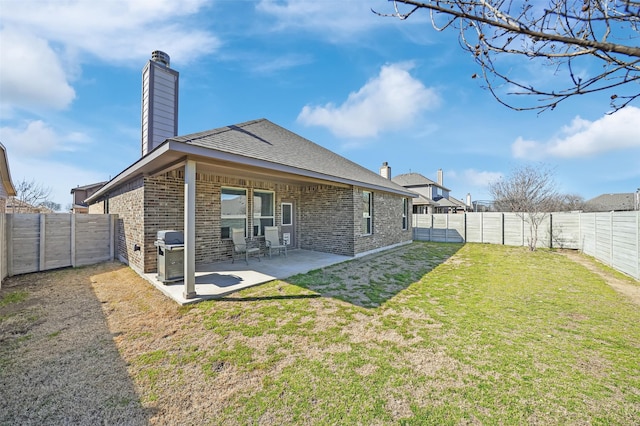 back of property with a fenced backyard, brick siding, a lawn, a chimney, and a patio area