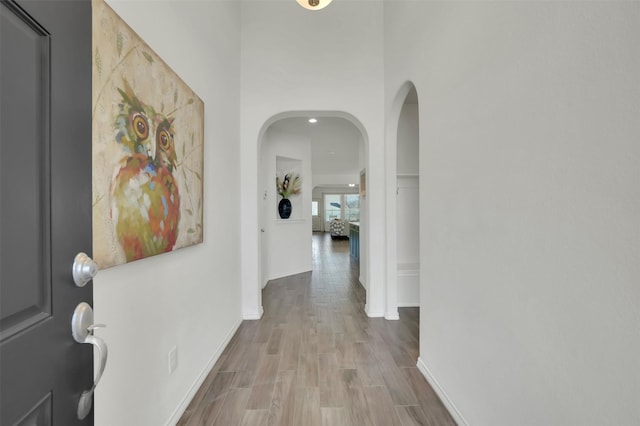 corridor with arched walkways, wood finished floors, and baseboards