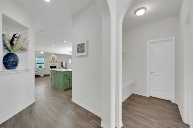 corridor with arched walkways, recessed lighting, baseboards, and wood finished floors