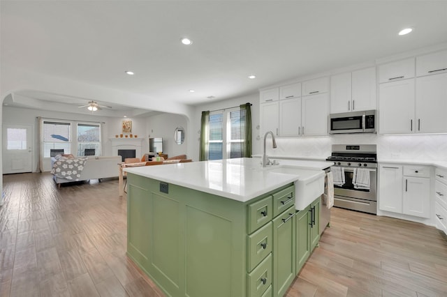 kitchen featuring a fireplace, green cabinets, appliances with stainless steel finishes, white cabinets, and a sink