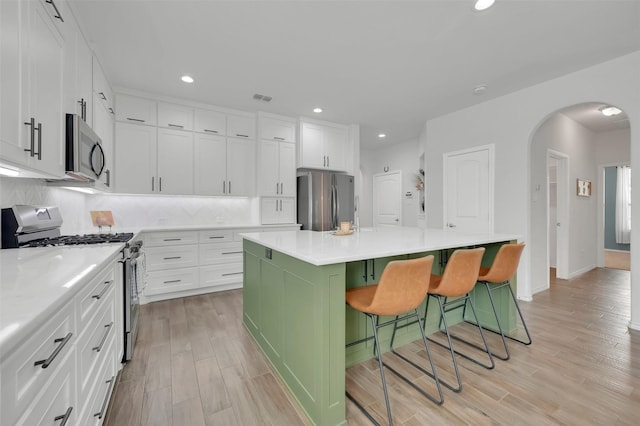 kitchen featuring arched walkways, stainless steel appliances, a breakfast bar, visible vents, and backsplash