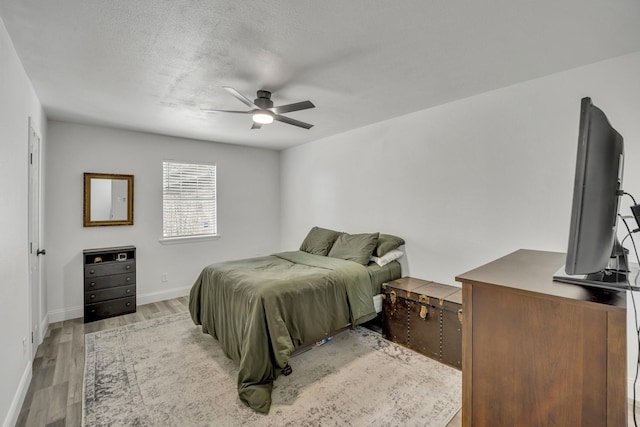 bedroom with light wood-type flooring, ceiling fan, and a textured ceiling