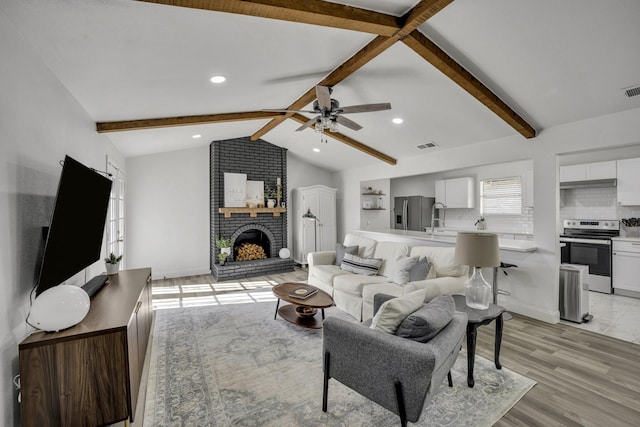 living room with light wood-type flooring, ceiling fan, lofted ceiling with beams, and a fireplace