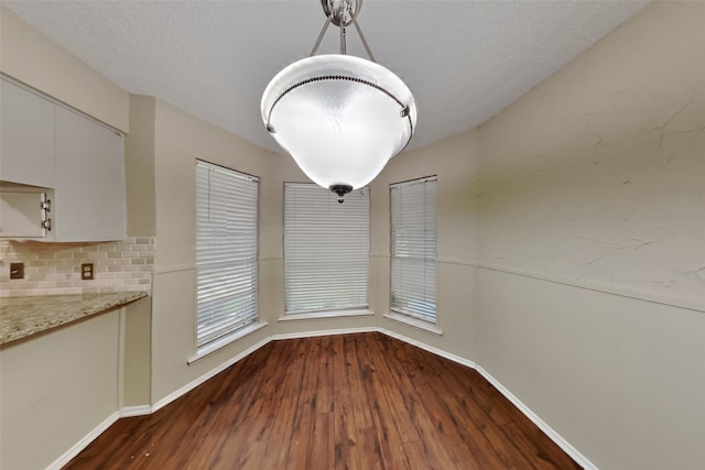 unfurnished dining area with dark wood-type flooring and a textured ceiling