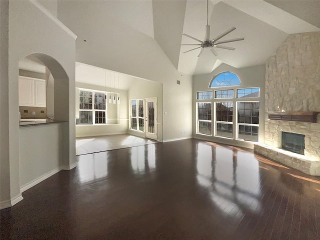 unfurnished living room featuring ceiling fan, high vaulted ceiling, hardwood / wood-style floors, and a stone fireplace